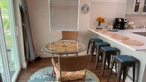 A kitchen with a round glass table, wicker chairs, and a bar area with stools.