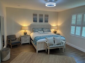 A bedroom with a bed, two nightstands, a chair, a window with blinds, and a ceiling fan.