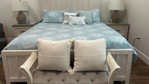 A bedroom with a bed, two nightstands, a chair, and three wall-mounted paintings.