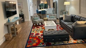 A modern living room with a black leather sofa, grey armchairs, a white coffee table, and a colorful rug.