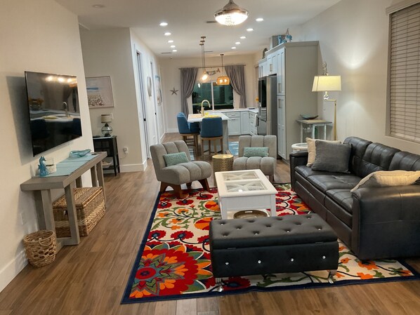 A modern living room with a black leather sofa, grey armchairs, a white coffee table, and a colorful rug.