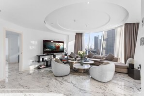 Un salon moderne doté d’un téléviseur à écran plat, de sièges confortables, d’une table basse et offrant une vue sur la ville.