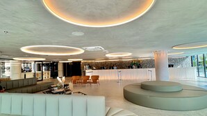 Un hall amplio de diseño moderno, con una gran zona de estar, mostrador de recepción y un techo único con iluminación circular.