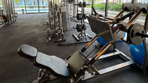 Un gimnasio moderno con varios equipos de ejercicio, ventanas amplias y vistas a la ciudad.