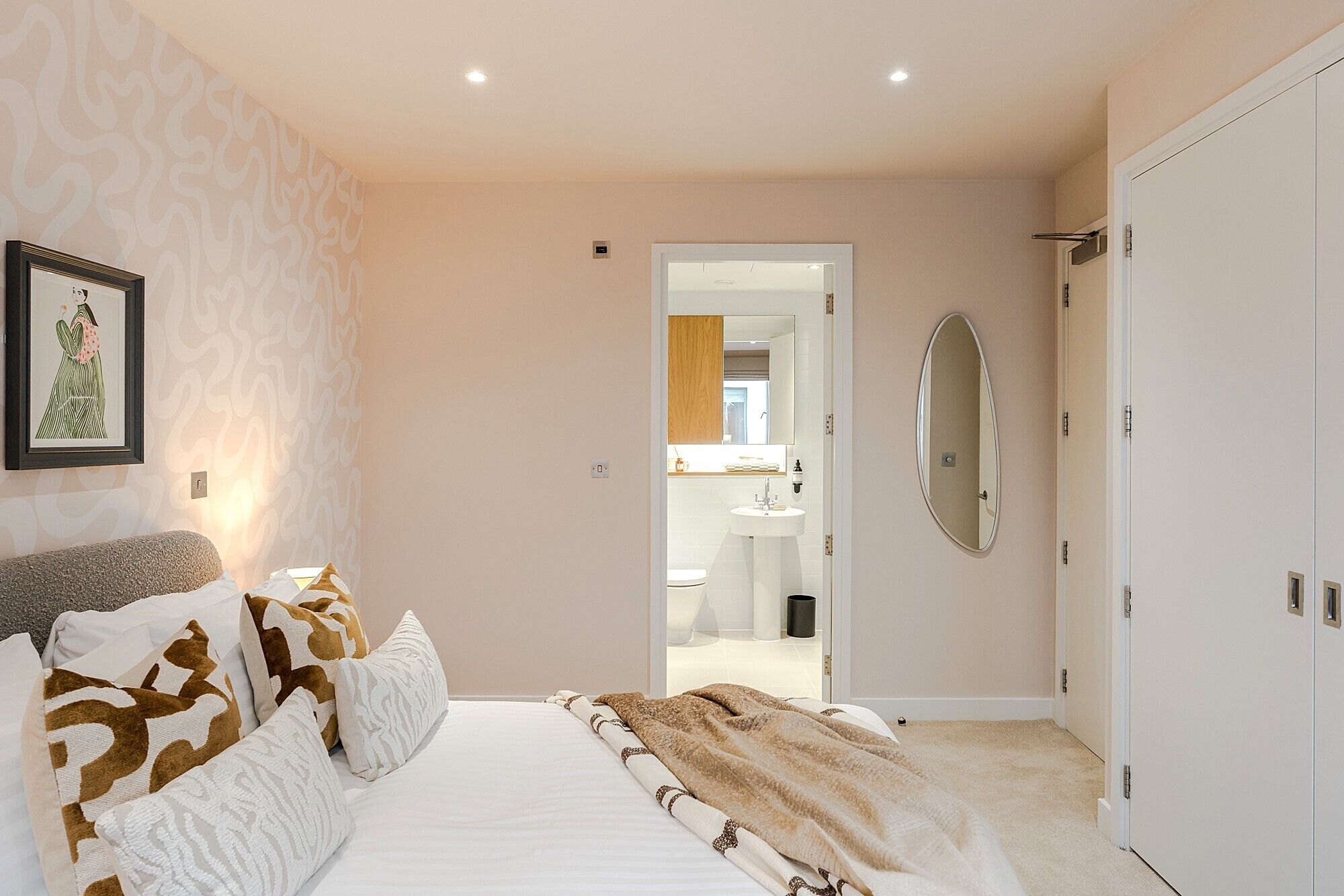 A bedroom with a bed, pillows, a mirror, and a door leading to a bathroom.