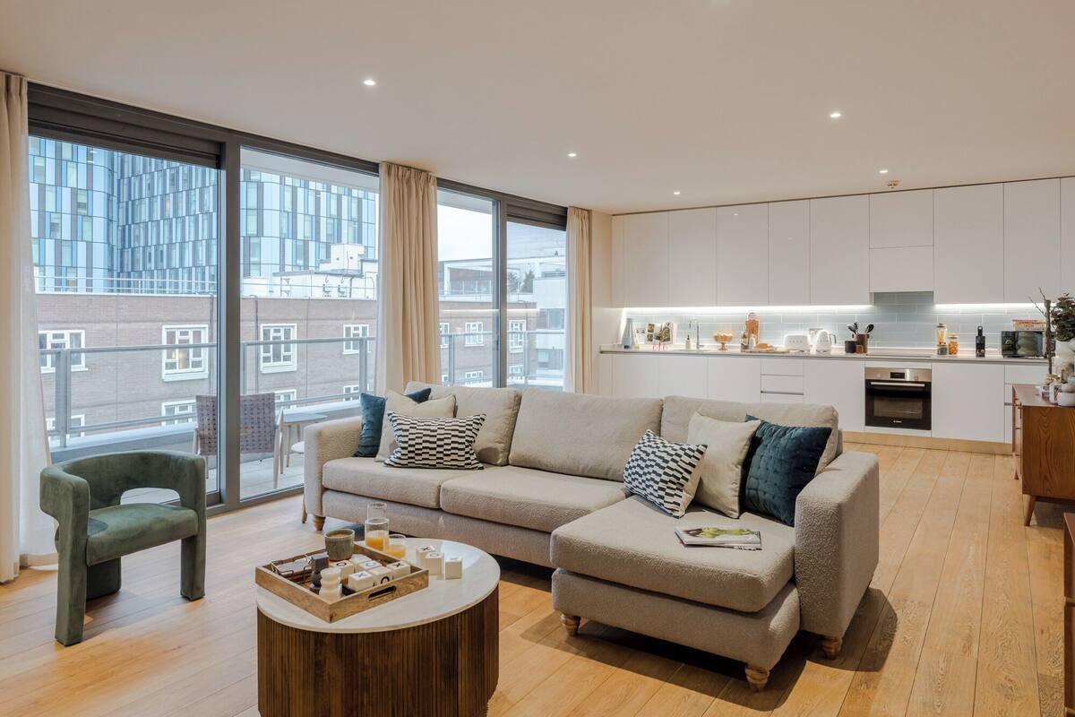 Eine moderne Wohnung mit einem großen Sofa, einem Couchtisch und Blick auf die Stadt durch große Fenster.