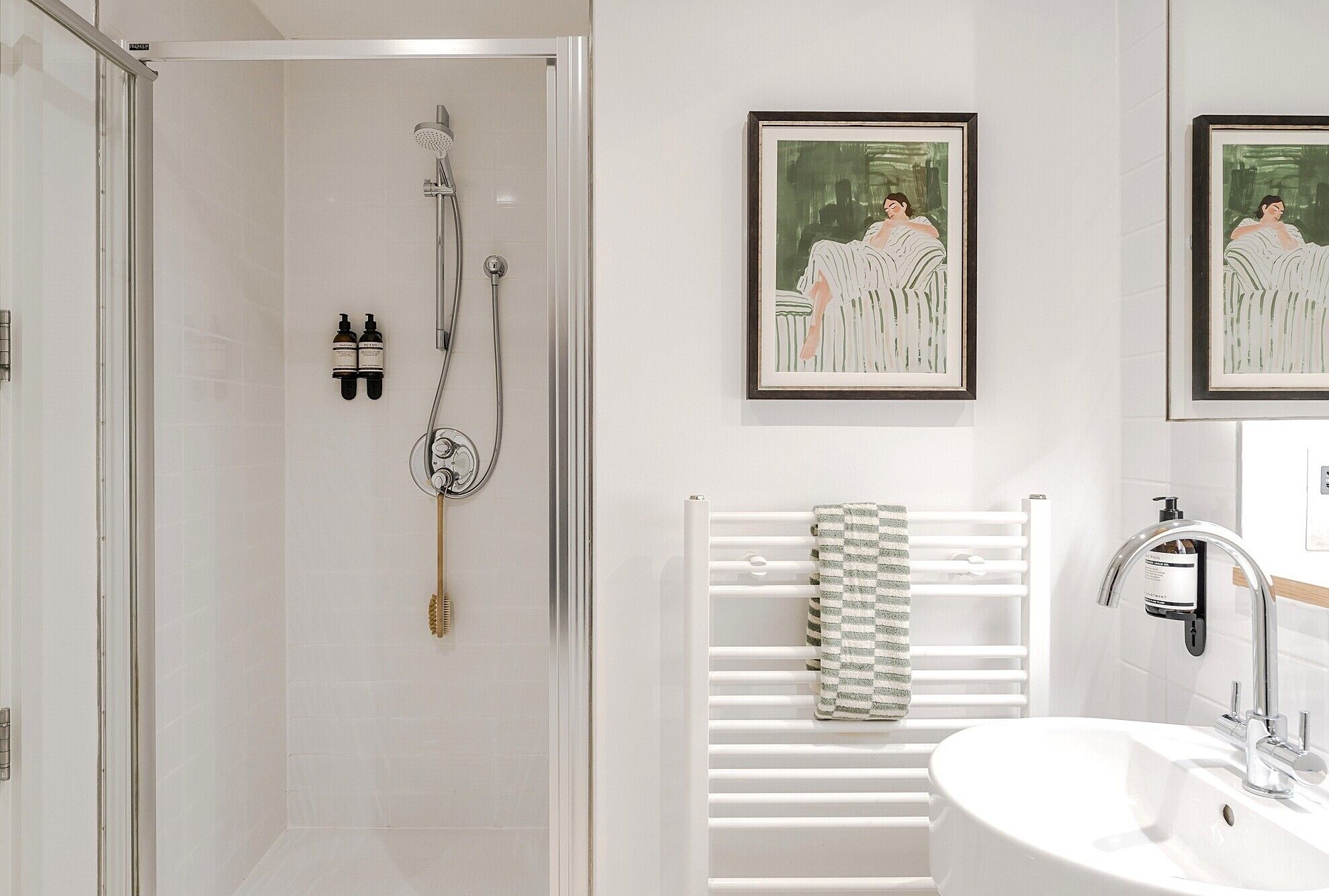 A modern bathroom with a shower, a sink, and two framed artworks on the wall.