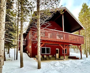 A cabin with a balcony, surrounded by trees and snow.