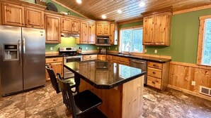 Una cocina con armarios de madera, un refrigerador de acero inoxidable, un microondas y una isla grande con encimera negra.