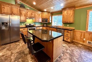 A kitchen with wooden cabinets, a stainless steel refrigerator, a microwave, and a large island with a black countertop.