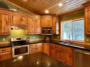 A kitchen with wooden cabinets, a granite countertop, a stove, a microwave, and a sink.