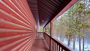 Un pasillo de madera con barandilla y vistas a un bosque nevado.
