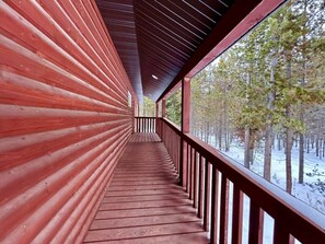 A wooden corridor with a railing, leading to a window overlooking a snowy forest.