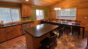 Interior de una cabaña de madera con cocina, comedor y un ventanal grande.