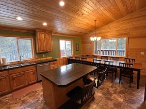 A wooden cabin interior with a kitchen, dining area, and a large window.