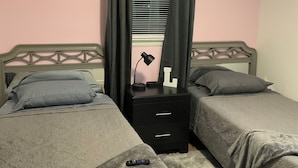 Ein Schlafzimmer mit zwei Einzelbetten, einem Nachttisch mit Lampe, einem Deckenventilator und einem Fenster mit Jalousien.