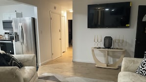 Ein Wohnzimmer mit beiger Couch, Couchtisch und an der Wand montiertem Fernseher.