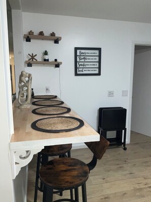 A dining area with a wooden table, four woven placemats, two dark wooden chairs, and a black chair with wheels. A motivational quote is displayed on the wall above the table.