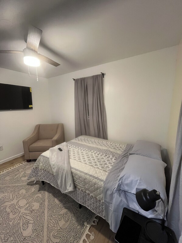 A bedroom with a bed, a chair, a ceiling fan, and a flat-screen TV.