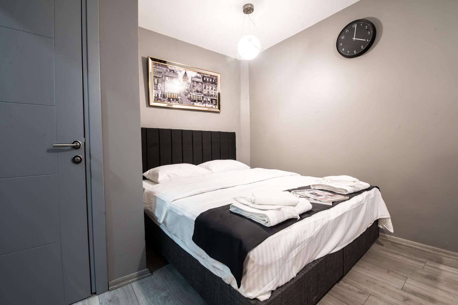 Een moderne slaapkamer met een bed, een ingelijst schilderij, een klok en een deur.