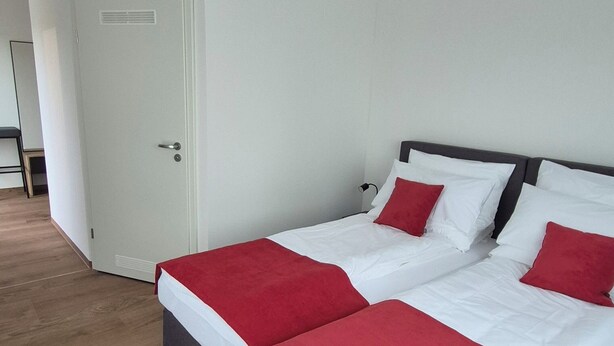 A hotel room with a large bed, a door, and a ceiling light fixture. - Apartments Seibel double/twin room with balcony (Reutlingen)