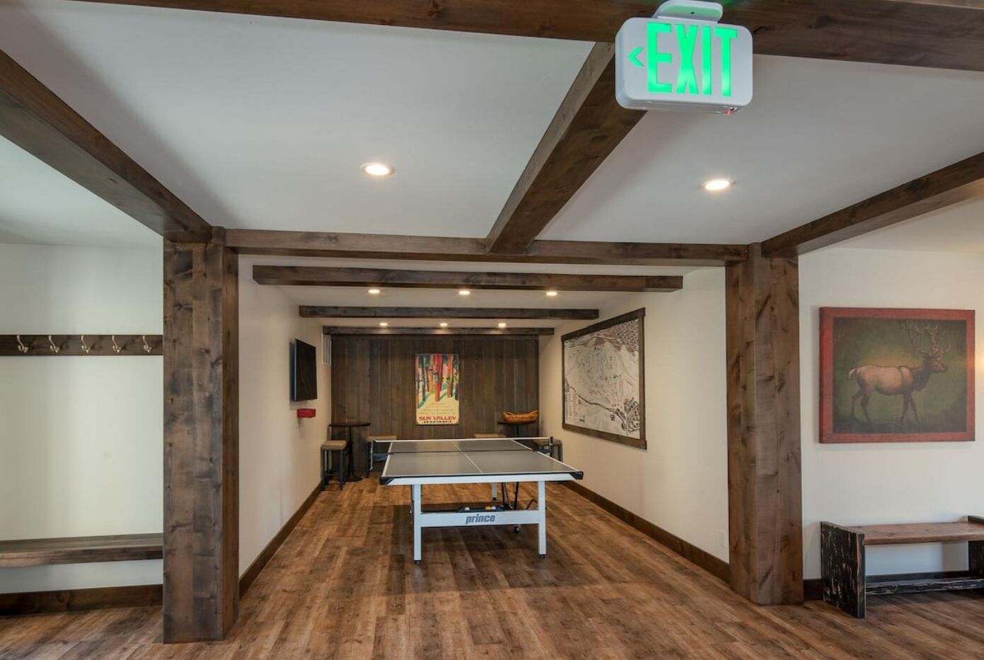 A room with a ping pong table, wooden beams, and a wall-mounted exit sign.