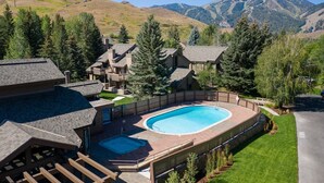 Área residencial com piscina, casas ao redor, deck de madeira e montanhas ao fundo.