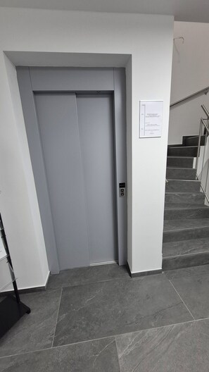 A modern elevator with a control panel, a staircase with metal railings, and a sign on the wall.