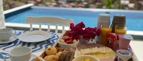 A breakfast tray with various foods and condiments by a poolside with a view of the ocean.