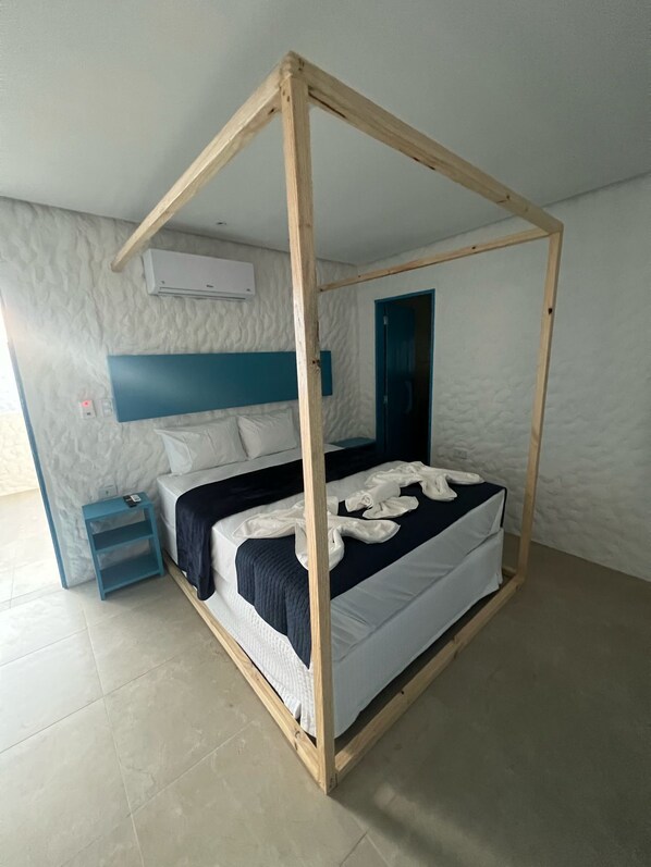Un lit à baldaquin avec du linge de lit blanc, une tête de lit bleue et une petite table de chevet avec une lampe.