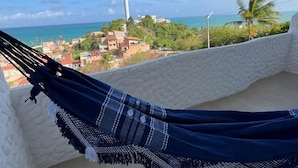 A hammock on a balcony with a view of a coastal town and a tall communication tower. - KEFI POUSADA (Maragogi)
