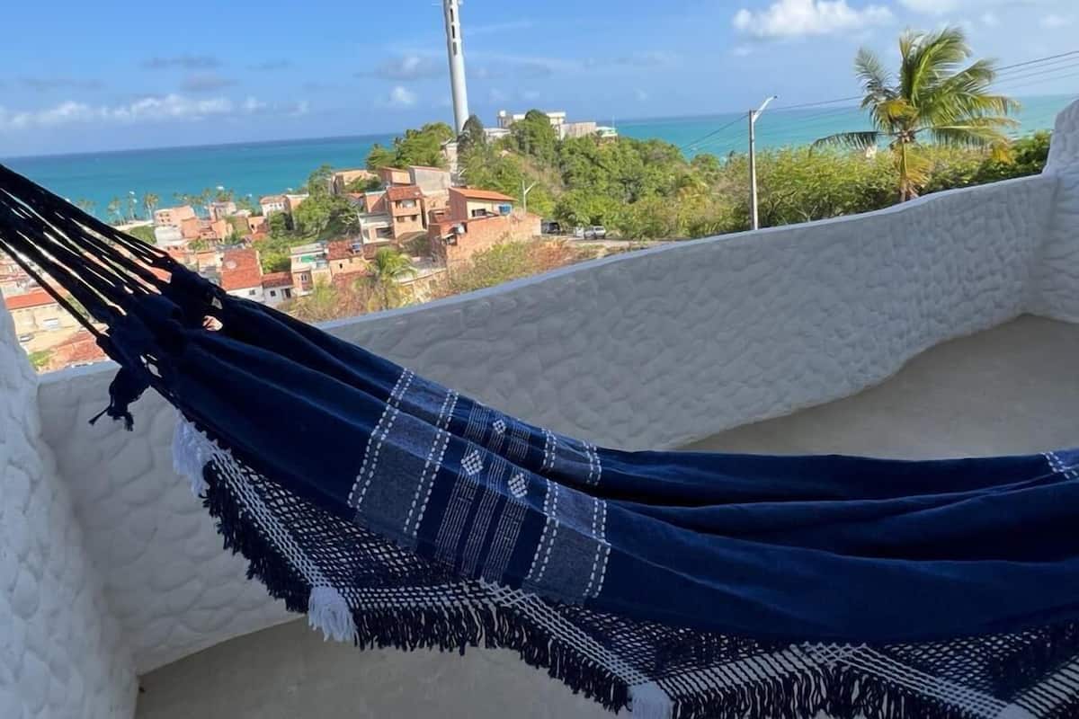 A hammock on a balcony with a view of a coastal town and a tall communication tower.