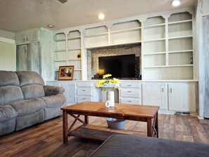 A living room with a sofa, a wooden coffee table with a vase of flowers, a television, and a fireplace.