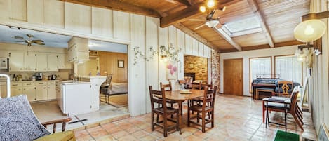 A spacious kitchen with wooden cabinets, a dining area with a wooden table and chairs, and a piano in the background.