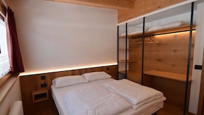 Ein modernes Schlafzimmer mit Holzkopfstütze, einem großen Bett mit weißer Bettwäsche, einem Nachttisch und einem Einbauschrank mit Kleiderstange.