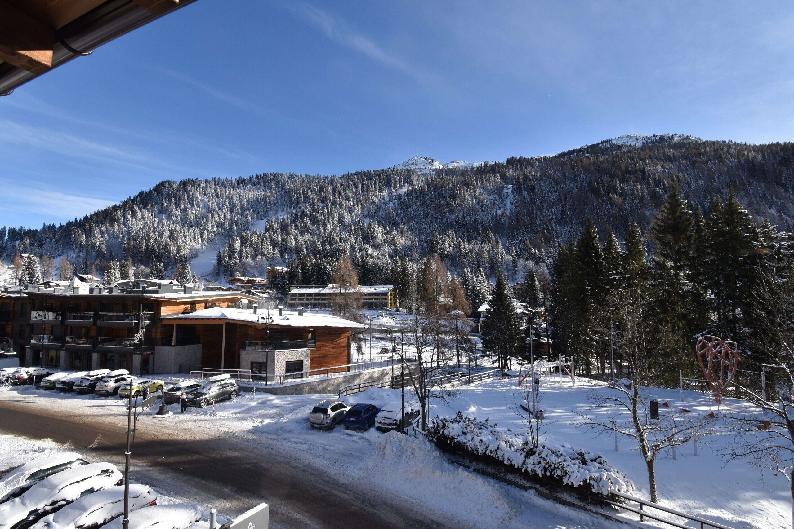 A snow-covered mountain with a ski resort, including a building with a wooden facade and parked cars.