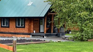 A log cabin with a green roof, a porch with outdoor seating, and a well-maintained lawn.