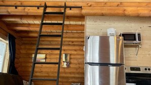 A wooden interior with a stainless steel refrigerator and oven, a ladder, and a couch.