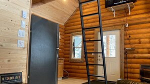 A log cabin interior with a wooden wall, a ladder, a door, a window, a television, and a sign that says "MEMORIES".