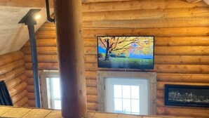 A log cabin interior with a large wooden beam, a mounted television, and a framed cityscape.