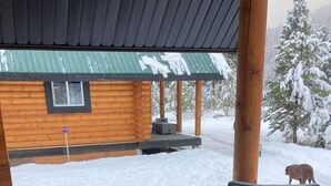 A covered outdoor seating area with wicker furniture and a view of a snowy landscape and a cabin.
