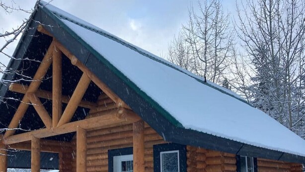 A log cabin with a snow-covered roof and a porch area.