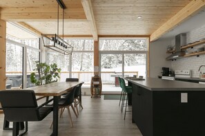 Eine moderne Küche mit Holzboden, großen Fenstern und einem Essbereich mit Holztisch und -stühlen.