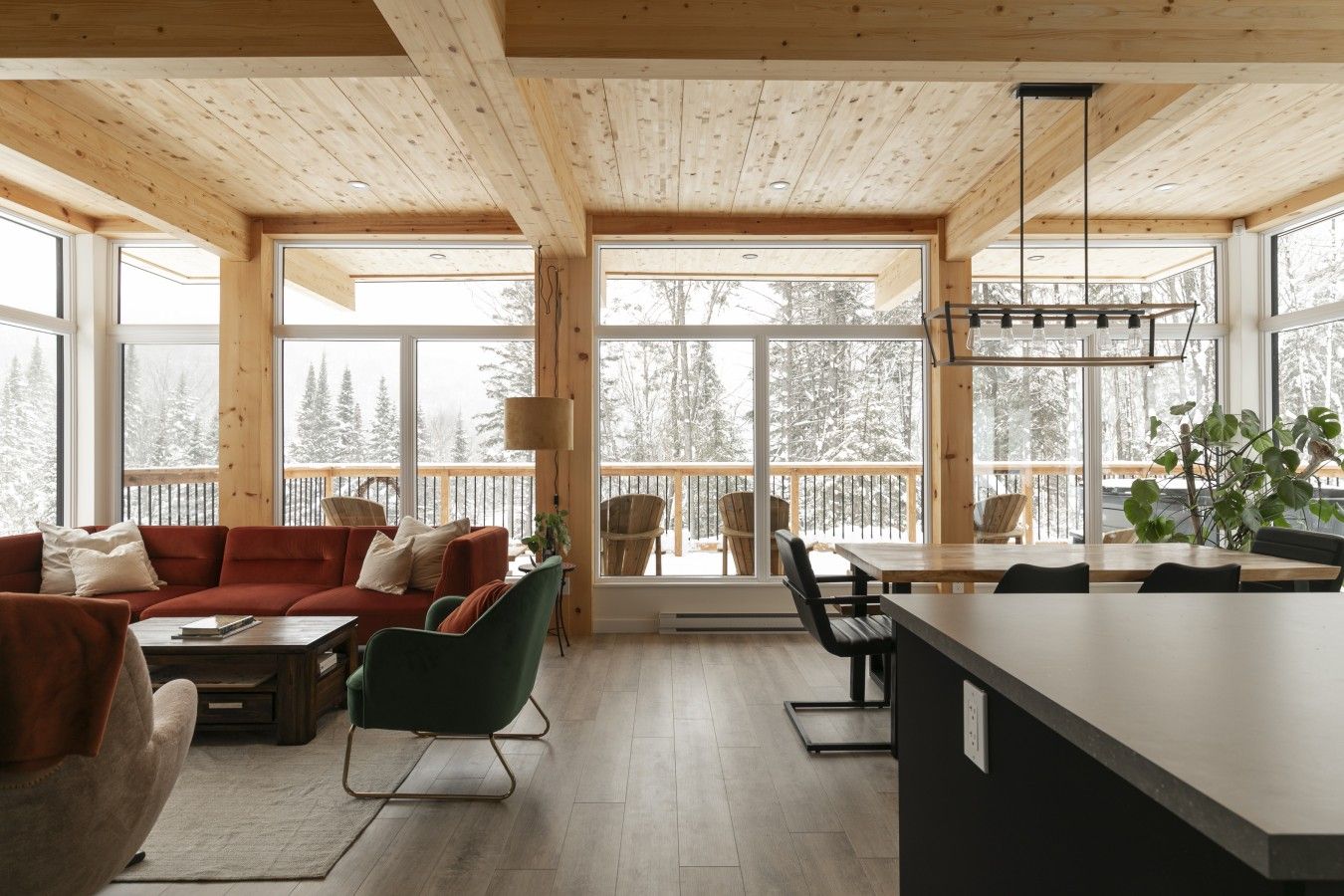 A modern interior with a wooden ceiling, large windows, a sofa, a dining table, and chairs.