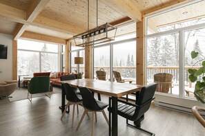 Ett rymligt rum med ett stort träbord, flera stolar och utsikt över en snötäckt skog genom stora fönster.