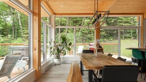 A spacious room with large windows, a wooden table, benches, and a potted plant.