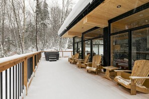 Ein mit Schnee bedeckter Deck mit Holzstühlen und einem Grill.