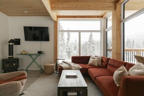 Ett mysigt vardagsrum med en öppen spis, en tv och ett stort fönster med utsikt över snötäckta träd.
