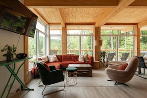 Un interior acogedor con techo de madera, ventanas amplias, un sofá modular, un sillón verde y una mesa de centro.
