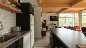 A modern kitchen with a wooden ceiling, a dining area with a large table, and a TV mounted on the wall.